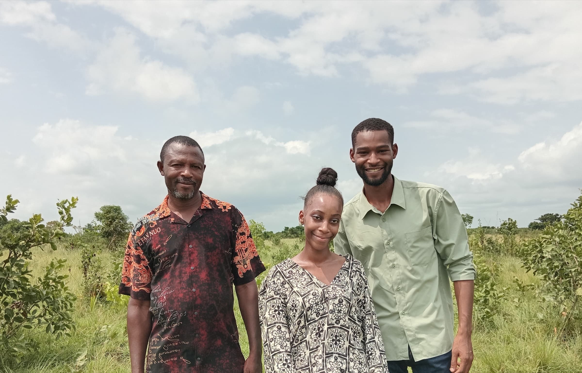 Three people, including Ubuntu Eco Gardens founder Kayode Ewuoso, standing together in the open grassland at the Phase One development site