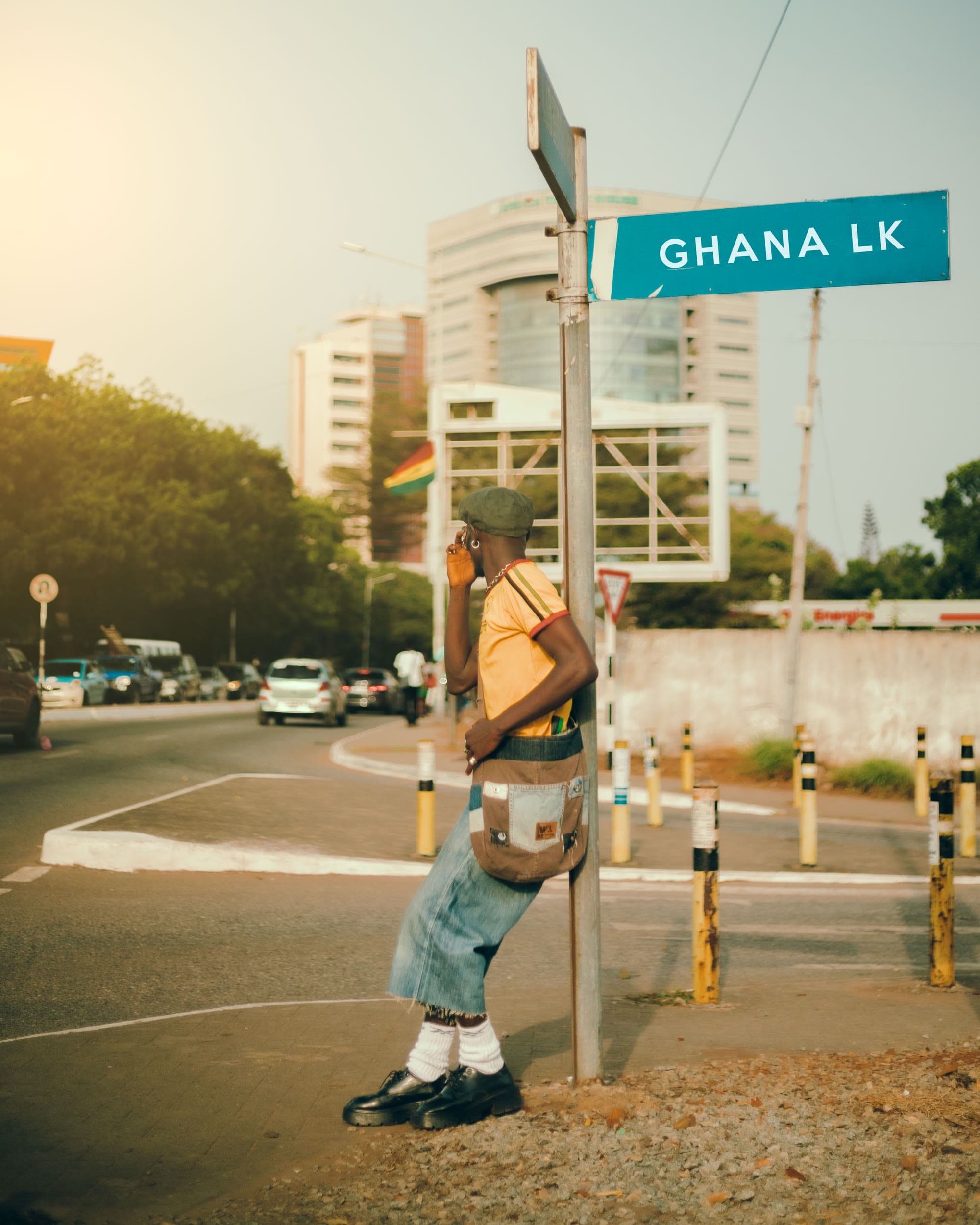 A young man in Accra pauses at a street corner beneath a Ghana road sign