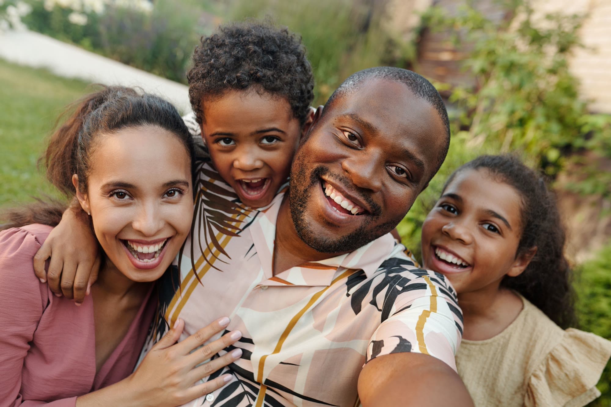 A family of four laughing together for a close-up selfie outdoors